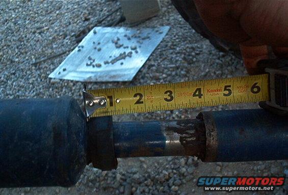 Tape measure held against a blue metal shaft or axle tube measuring approximately 3 inches diameter