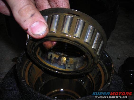 Hand holding a greasy wheel bearing over a housing