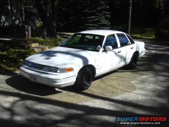 White sedan parked on a driveway, front 3/4 view. Black steel wheels, some shadows on the hood