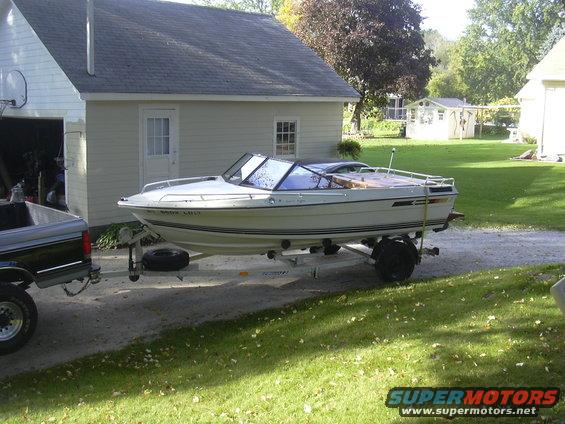 White boat with black trim on a trailer, side view, parked in a driveway next to a house
