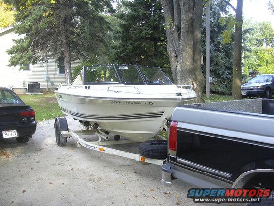 White boat on a trailer, with a black car and a pickup truck nearby
