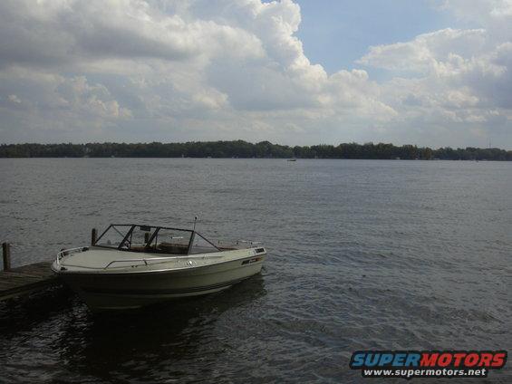 Boat docked on a wooden pier next to a calm lake with a tree line in the distance