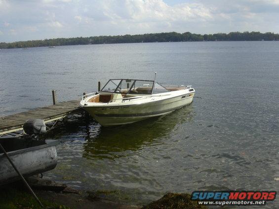 Cream-colored boat with a black windshield frame docked at a wooden pier. A smaller boat is partially visible to the left