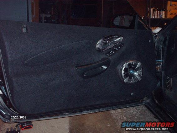Car door panel with aftermarket speaker and carbon fiber trim around window controls