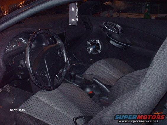 Car interior with cloth seats, aftermarket speaker, and a bandana hanging from the rearview mirror