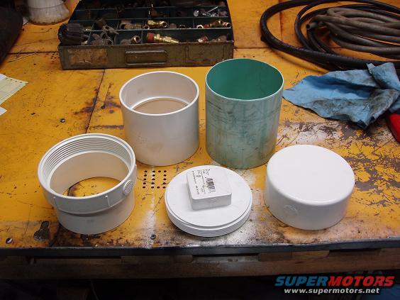 PVC pipe fittings and caps on a yellow workbench with a toolbox and hose in the background