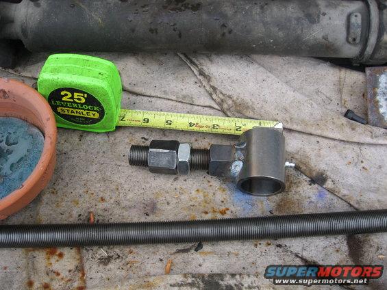 Close-up of a threaded rod assembly next to a tape measure and a small pot