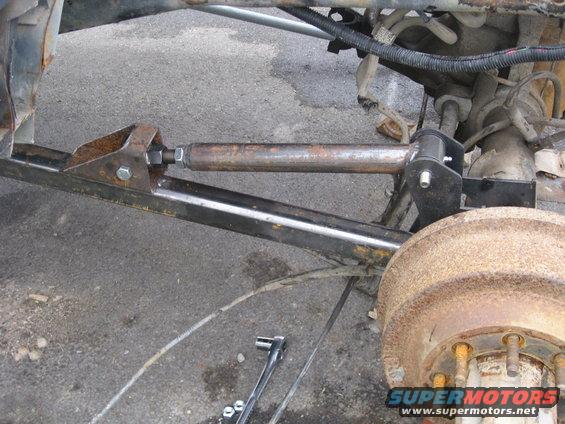 Close-up of a custom steering linkage installed on a truck's rear axle, with a drum brake visible