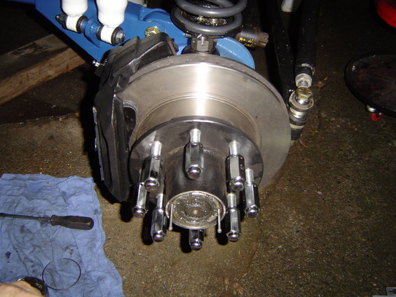 Front wheel hub with 8 lug nuts and brake caliper. Blue suspension components visible