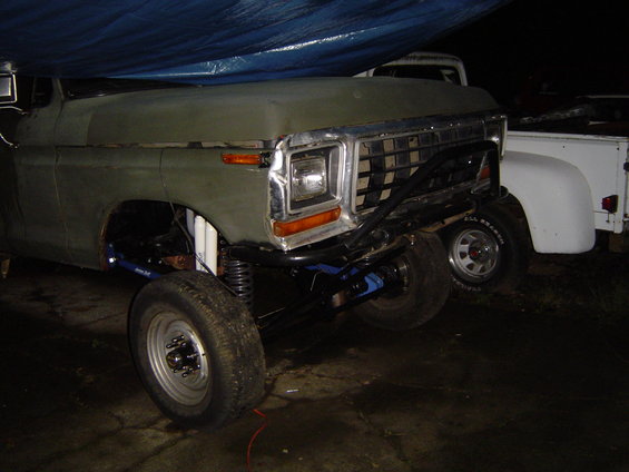 Front of a lifted truck with a custom bumper and aftermarket suspension. Another white truck is visible behind it