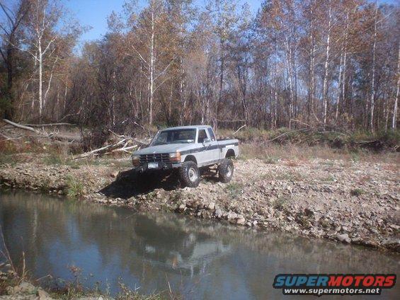 Lifted pickup truck parked by a stream with trees in the background