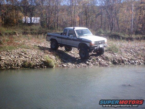 1990 Ford Ranger pickup truck with lift kit parked on a rocky shore next to water