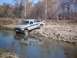 1990 Ford Ranger - A lifted pickup truck navigates a rocky stream bed, its tires partially submerged in the water.