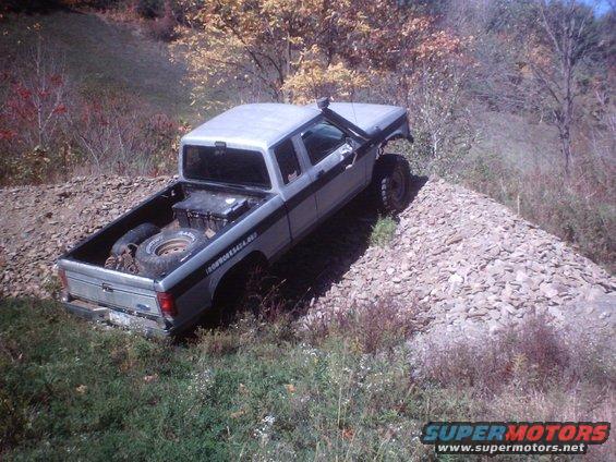 1990 Ford Ranger pickup truck with a snorkel, lifted suspension, and spare tire in the bed, driving on a rocky incline