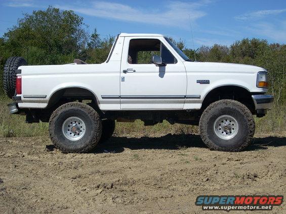 White 1992 Ford Bronco parked on dirt with trees in background
