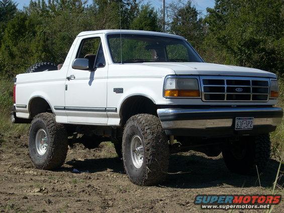 White 1992 Ford Bronco with lifted suspension and large off-road tires, parked on dirt