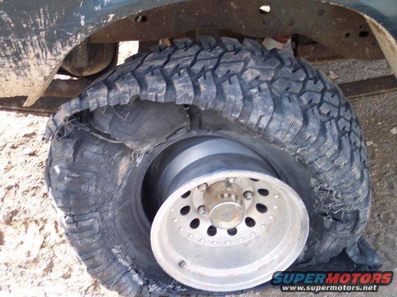 Shredded tire and rim on a vehicle, showing damage