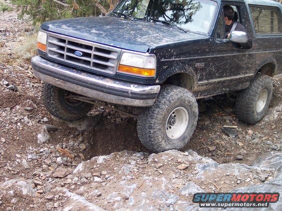 Ford Bronco navigating rocky terrain, front wheel in a hole
