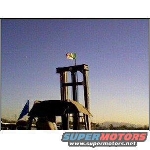 Wooden structure with a flag against a clear blue sky. Supermotors.net logo visible