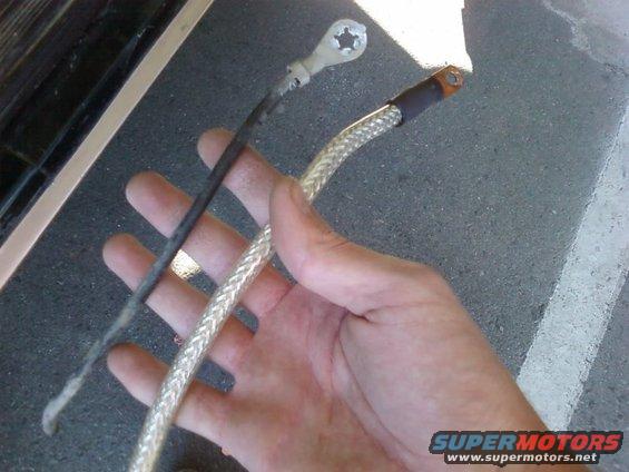 Hand holding old battery cable next to a braided replacement cable