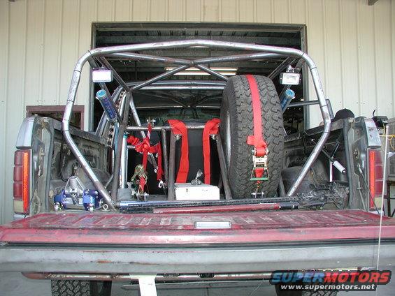 Rear view of a pickup truck bed modified with a roll cage, spare tire, and straps