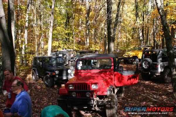 Red Jeep Wrangler with open door, black Jeep Cherokee, and yellow Jeep in autumn forest