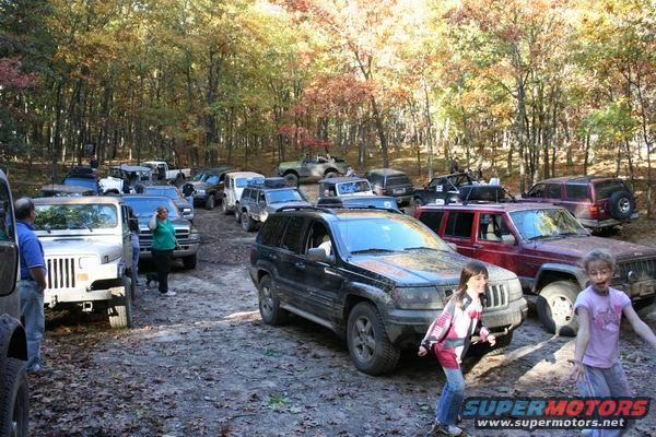 Black Jeep Grand Cherokee, 3q-front view, parked in woods with other vehicles