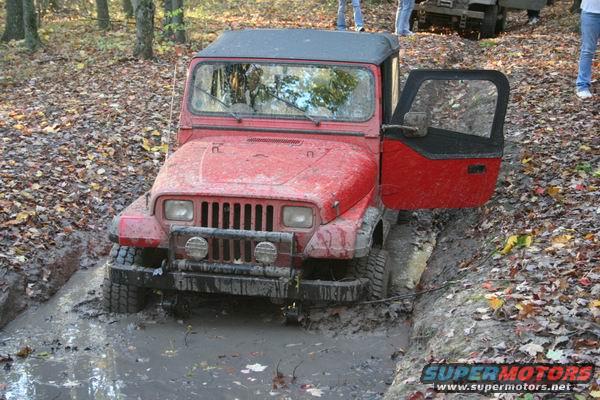 Red Jeep Wrangler with door open stuck in a muddy trail in the woods