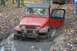 1992 Jeep Cherokee - A red Jeep Wrangler navigates a muddy off-road trail, its door ajar.