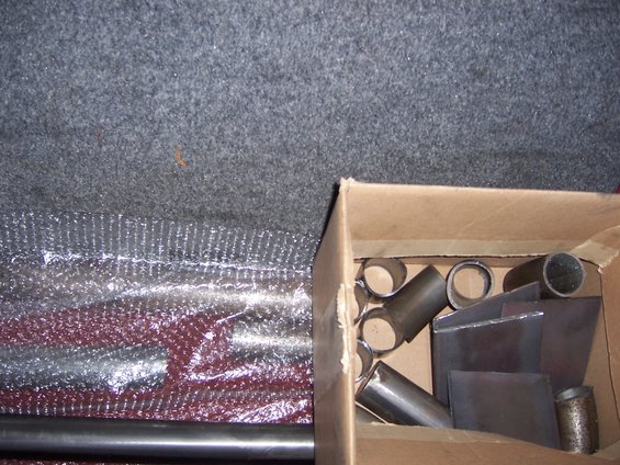Cardboard box with metal tubes and flat plates, some wrapped in bubble wrap