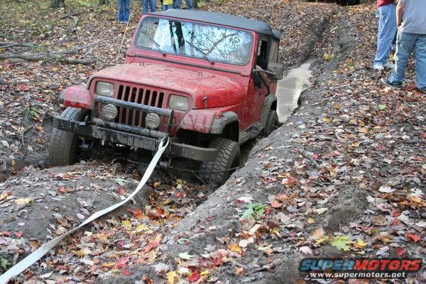 Red Jeep Wrangler stuck in a muddy ditch, with a tow strap attached to the front bumper