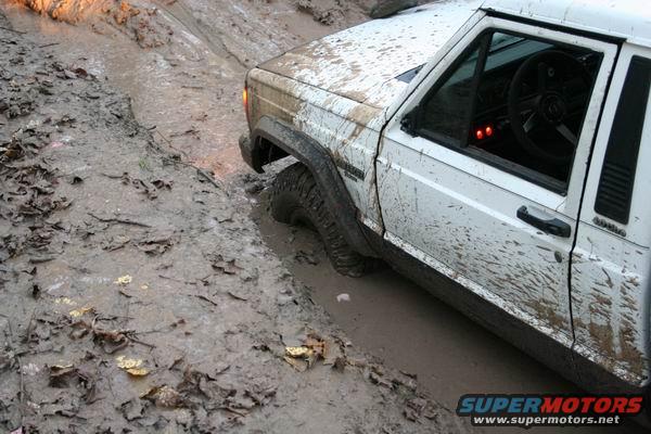 White 1992 Jeep Cherokee stuck in mud, front wheel deep in mire