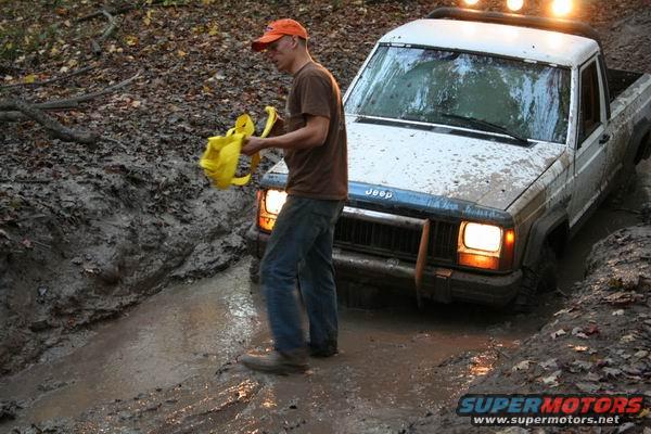 1992 Jeep pickup truck stuck in mud with a person holding a yellow object