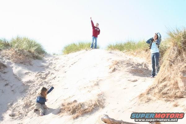 Three children on sand dunes with beach grass under a bright sky