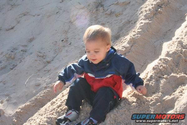 Child in red, white, and blue jacket playing in sand dunes