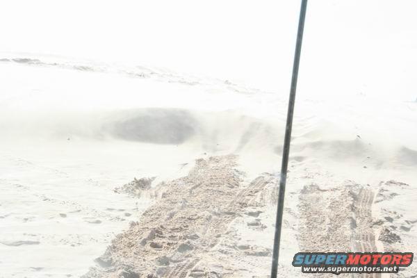 Tire tracks in sand dunes with a vertical pole on the right
