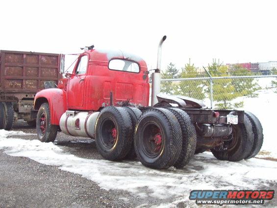 Red semi-truck tractor with dual rear wheels, towing a rusty dump trailer. Visible text on trailer