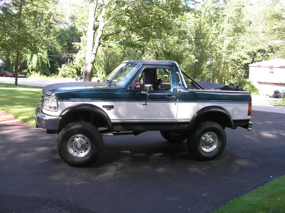 Green and white Ford Bronco with aftermarket wheels and tires, lifted suspension, and a roll bar