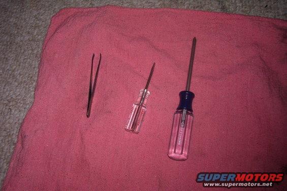 Tweezers and two screwdrivers on a pink cloth. One screwdriver has 'CRAFTSMAN' visible