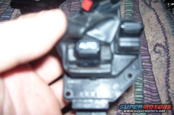 Close-up of an automotive light switch with an 'AUTO' button. A hand is visible on the left