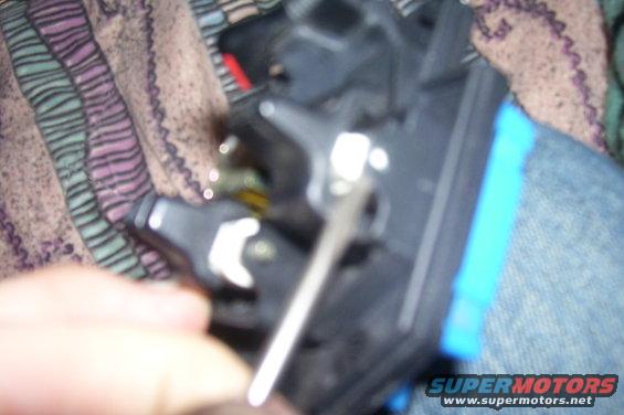 Close-up of a black car part with a silver tool, blue tape visible