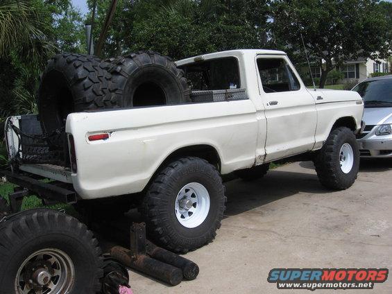 White pickup truck with oversized tires in the bed and on the ground. Truck has a lifted suspension
