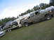 1979 Ford F-150 - A camouflaged Ford F-250 truck is seen from the side, towing a trailer carrying another pickup truck.