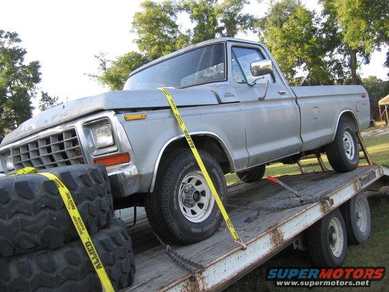 Silver 1979 Ford F-150 on a flatbed trailer, secured with yellow straps. Tires are stacked on the left