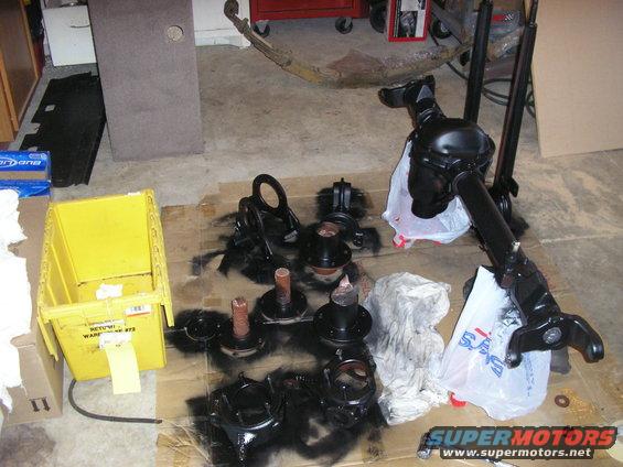 Various black automotive parts, including a differential and hubs, laid out on cardboard on a garage floor