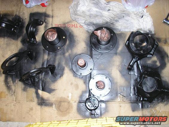 several black automotive parts laid out on cardboard, some with copper-colored centers