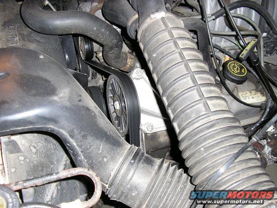 Close-up of engine bay showing ribbed air intake hose, belts, and pulleys