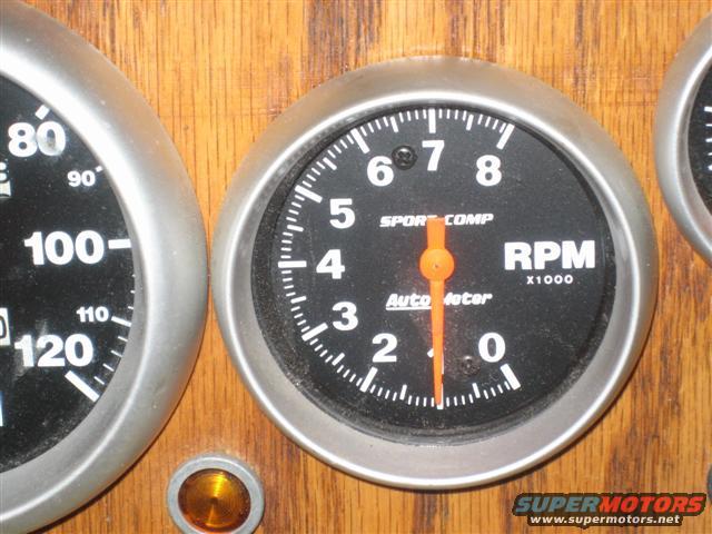 Dashboard with a tachometer and speedometer gauges mounted on wood paneling