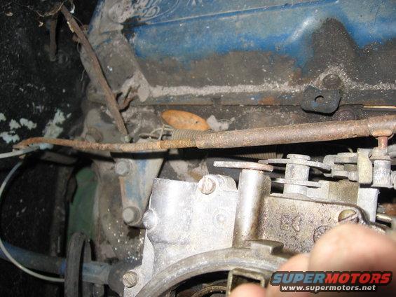 Close-up of a carburetor with linkage and engine components visible. Watermark says SUPERMOTORS