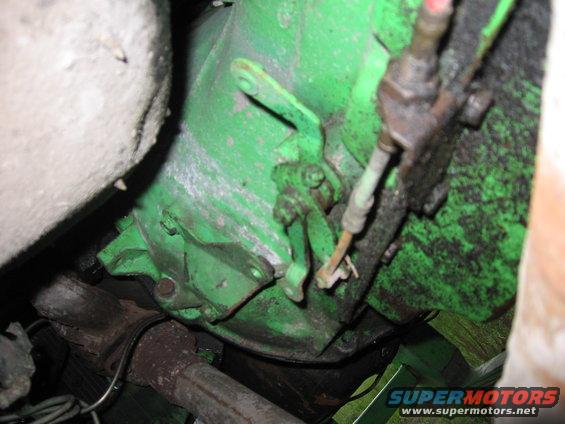 close-up of a green transmission housing with linkage and exhaust pipe visible